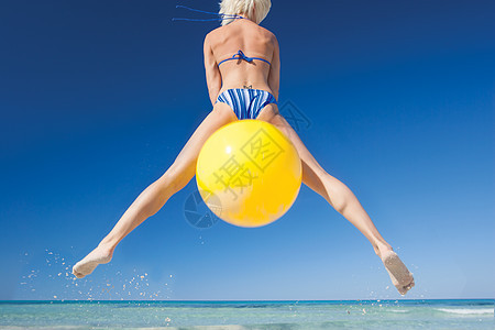 年轻女在西班牙海滩的空中带着球跳跃图片