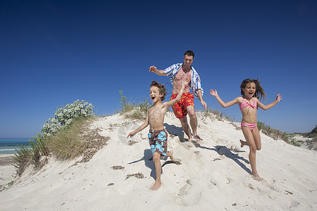 父亲与儿女一起在西班牙海滩沙丘上奔跑图片