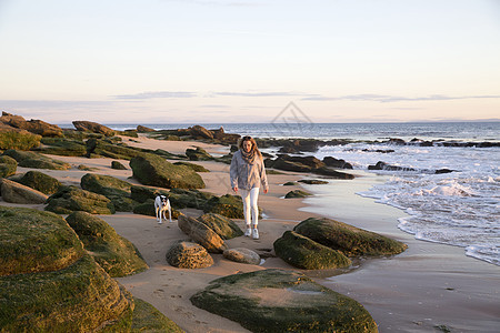 在西班牙特拉法加尔角岩石海滩上行走的女人和宠物狗图片