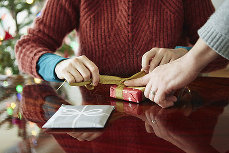 在餐桌上包着圣诞礼物的夫妇双手被裁剪的一张照片图片
