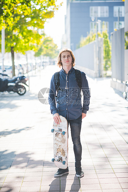 站在人行道上充满自信的年轻男城市滑板运动员的肖像图片
