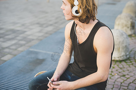 坐在人行道边戴着耳机听音乐的年轻人图片
