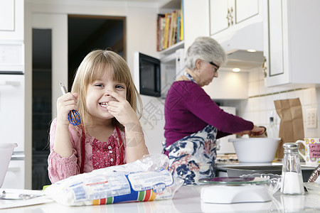 女孩与祖母一起做饭时拿着剪刀微笑图片