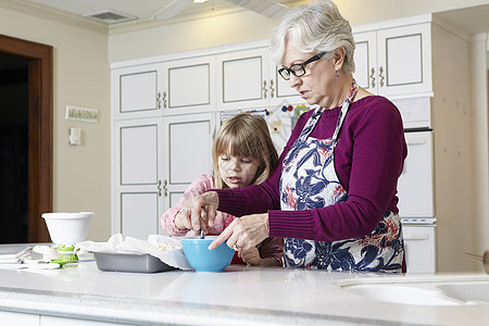女孩和祖母在厨房柜台搅拌蛋糕糊图片