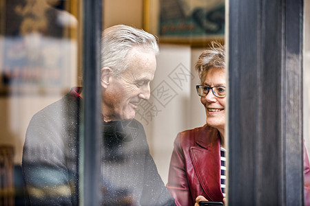 坐在咖啡馆窗口座位聊天的年长夫妇图片