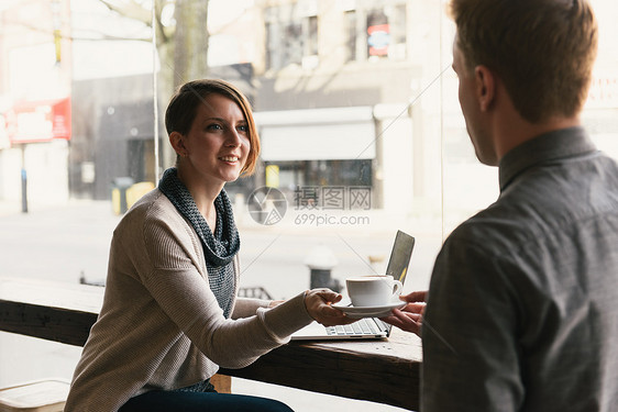 向坐在咖啡店窗口的女顾客提供咖啡的服务员图片