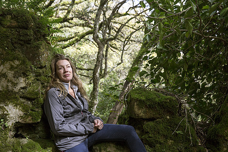 在林地岩石上坐着休息的女徒步旅行者图片