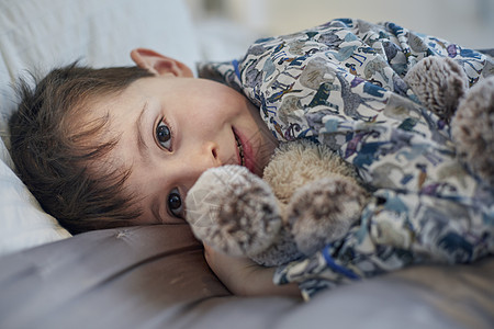 穿着睡衣的小男孩抱着娃娃躺在床上图片