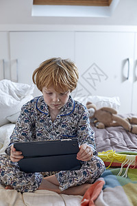 穿睡衣的男孩在床上使用数字平板电脑图片
