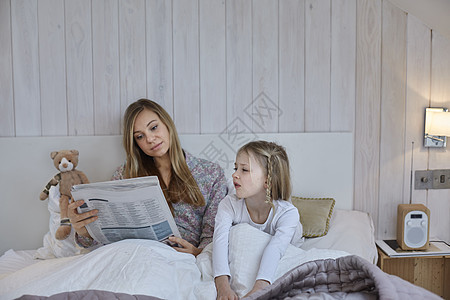 母亲躺在女儿旁边阅读报纸图片