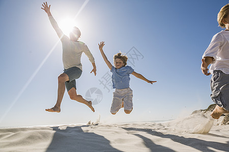 父亲和儿子在沙滩上手臂举起跳跃图片