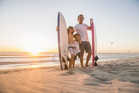 父亲和儿子在日落时站海滩上持冲浪板拍照图片