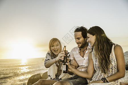 南非开普敦三位中年朋友坐在日落的海滩上举杯图片