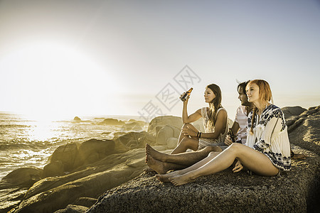 三名中年成人坐在海滩上看着日落图片