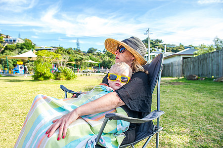 在新西兰Waiheke岛公园男孩在母亲大腿上坐着晒太阳图片