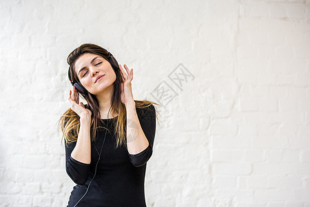 美丽的年轻女子在白墙前沉浸式听耳机音乐图片