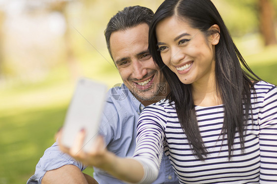坐在草地上用智能手机自拍的情侣图片