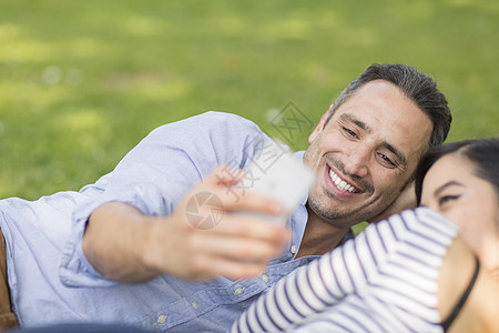 躺在草地上的情侣使用智能手机自拍图片