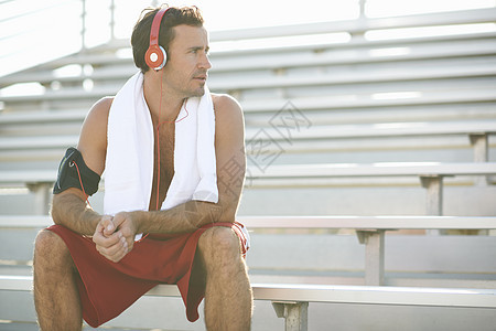 中年男子坐在长凳上休息戴耳机用毛巾围着颈部图片