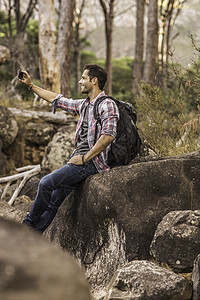 坐在岩石上使用手机拍照的徒步旅行者图片