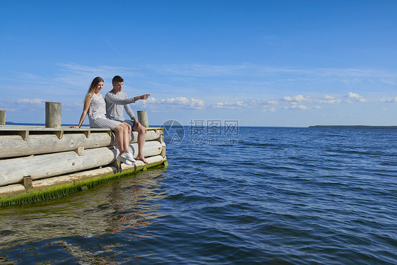 年轻夫妇坐在木码头上看海聊天图片