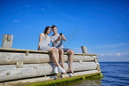 坐在木码头的一对夫妇用智能手机自拍图片