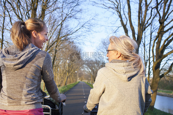 两个妇女在道路上骑自行车的背影图片