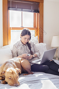 狗狗陪着正在使用电脑的主人一起坐在床上图片