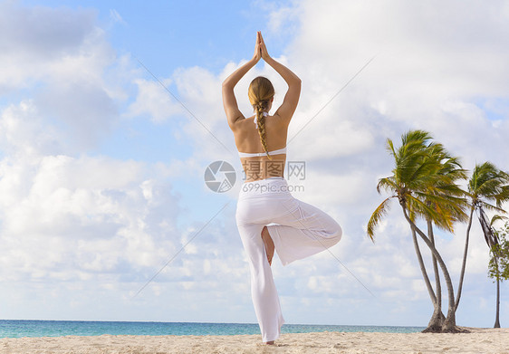在多米尼加勒比海滩上做瑜伽树姿势的年轻女子图片