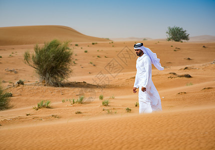 阿拉伯联合酋长国迪拜身着传统服装的中东男子在沙漠行走图片