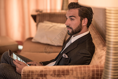 青年商人坐在旅馆沙发上使用数字平板电脑图片
