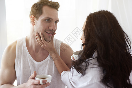 年轻夫妇在床上拿着咖啡微笑对视图片