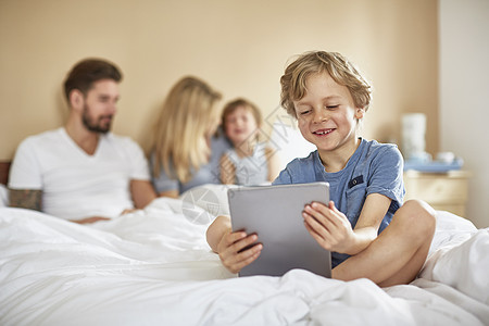男孩在父母床上笑着使用数字平板电脑的男孩图片