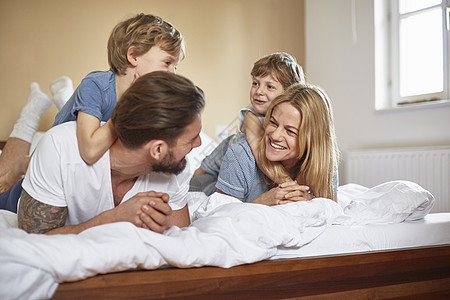 躺在父母顶上面对微笑的男孩在床上图片
