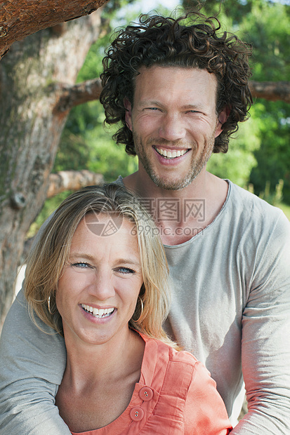 一对夫妇站在树旁微笑着看着摄像机图片