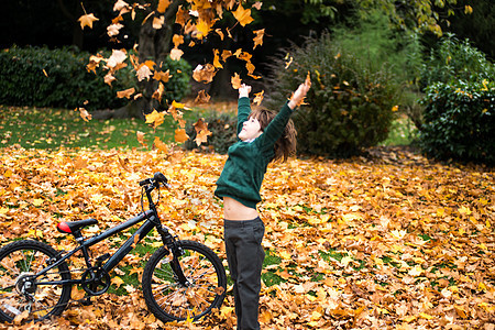 男孩在公园骑自行车扔秋叶图片