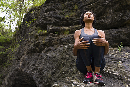 坐在岩石上抱膝冥想的女人图片