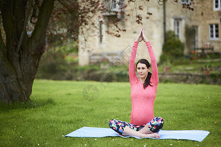 孕妇坐在草坪上的瑜伽垫子上练瑜伽图片