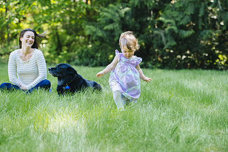 母亲带着狗狗和女儿在草地上玩耍图片