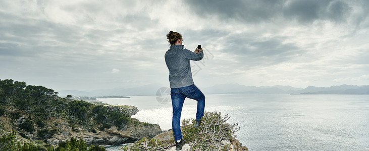 用手机拍摄悬崖照片的年轻人图片