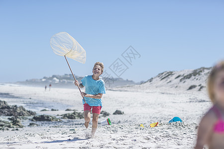 男孩在南非开普敦带渔网在海滩上奔跑图片