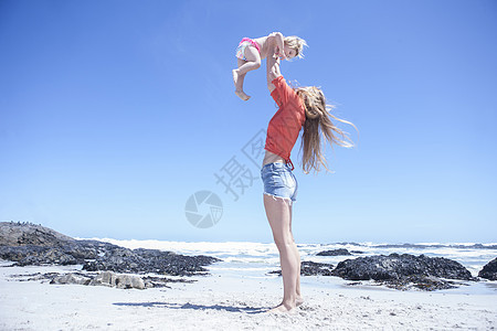 在海滩上抱女幼儿的年轻女子图片