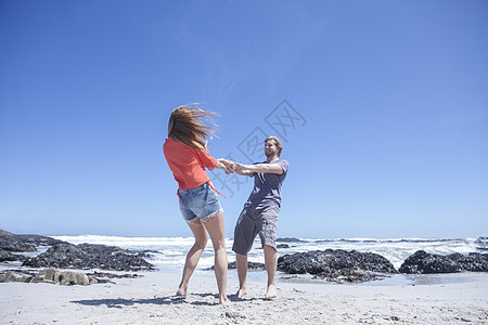 在海滩上年轻夫妇手牵手旋转图片