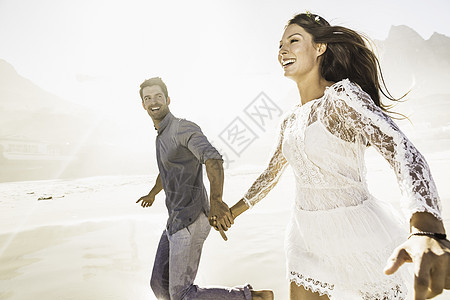 在南非开普敦的日光海滩上手牵奔跑的情侣图片
