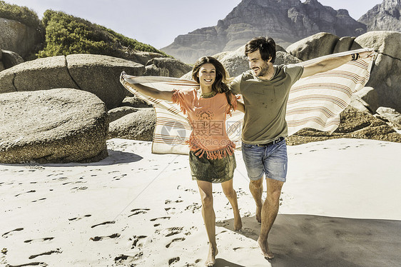 在海滩上拖着毯子跑来跑去的夫妇图片