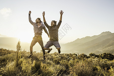 草地上举起手跳跃的两位男士图片