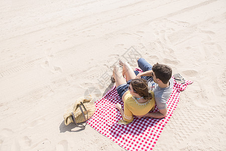 一对情侣躺在海滩上的野餐毯上休息看风景图片