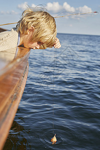 男孩趴在船边看漂浮的鱼图片
