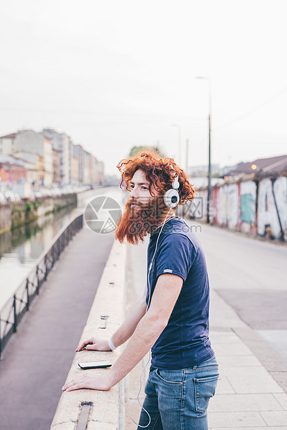 留着红头发和胡子的年轻男士在桥上戴着耳机听音乐图片