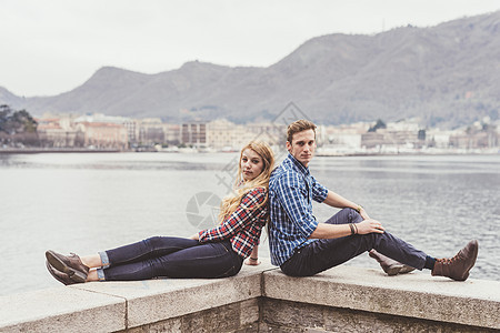 意大利科莫湖港口背靠背坐着的一对年轻夫妇图片